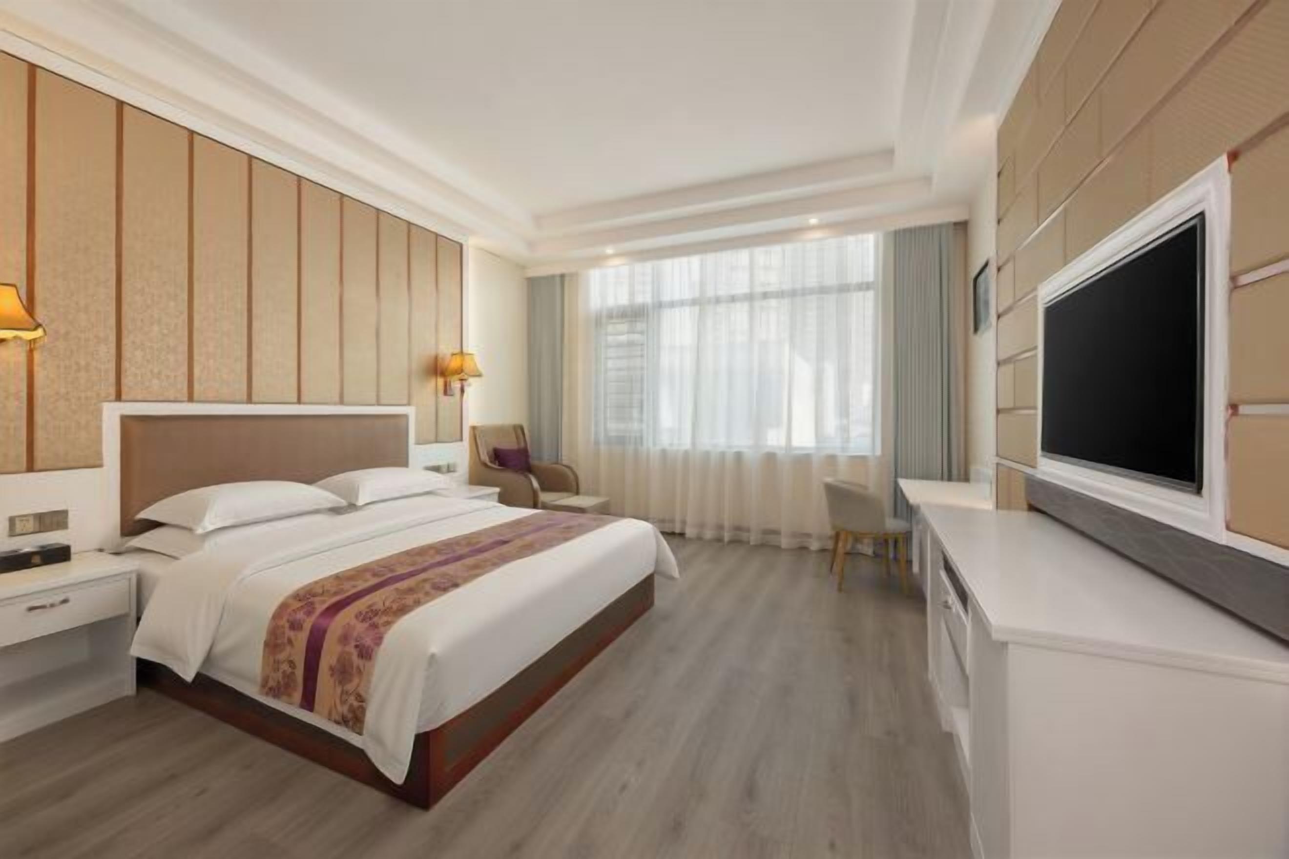 A hotel room with a large bed, bedside tables, a desk, and a TV.
