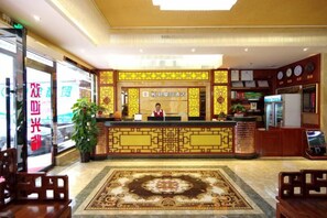 A hotel reception area with a reception desk, a large carpet, and a plant.