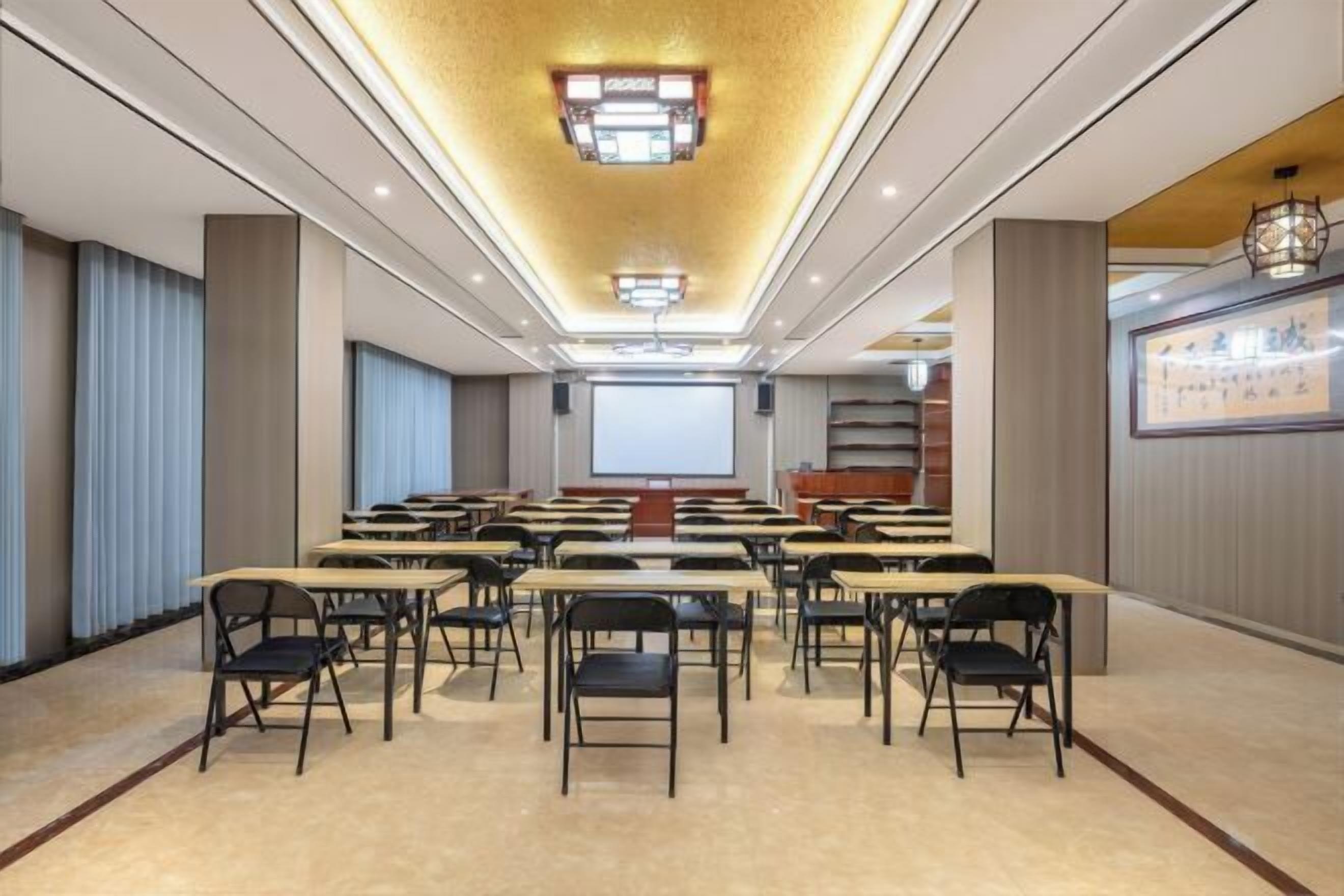 A conference room with tables and chairs arranged for meetings, a large screen at the front, and a ceiling with recessed lighting.