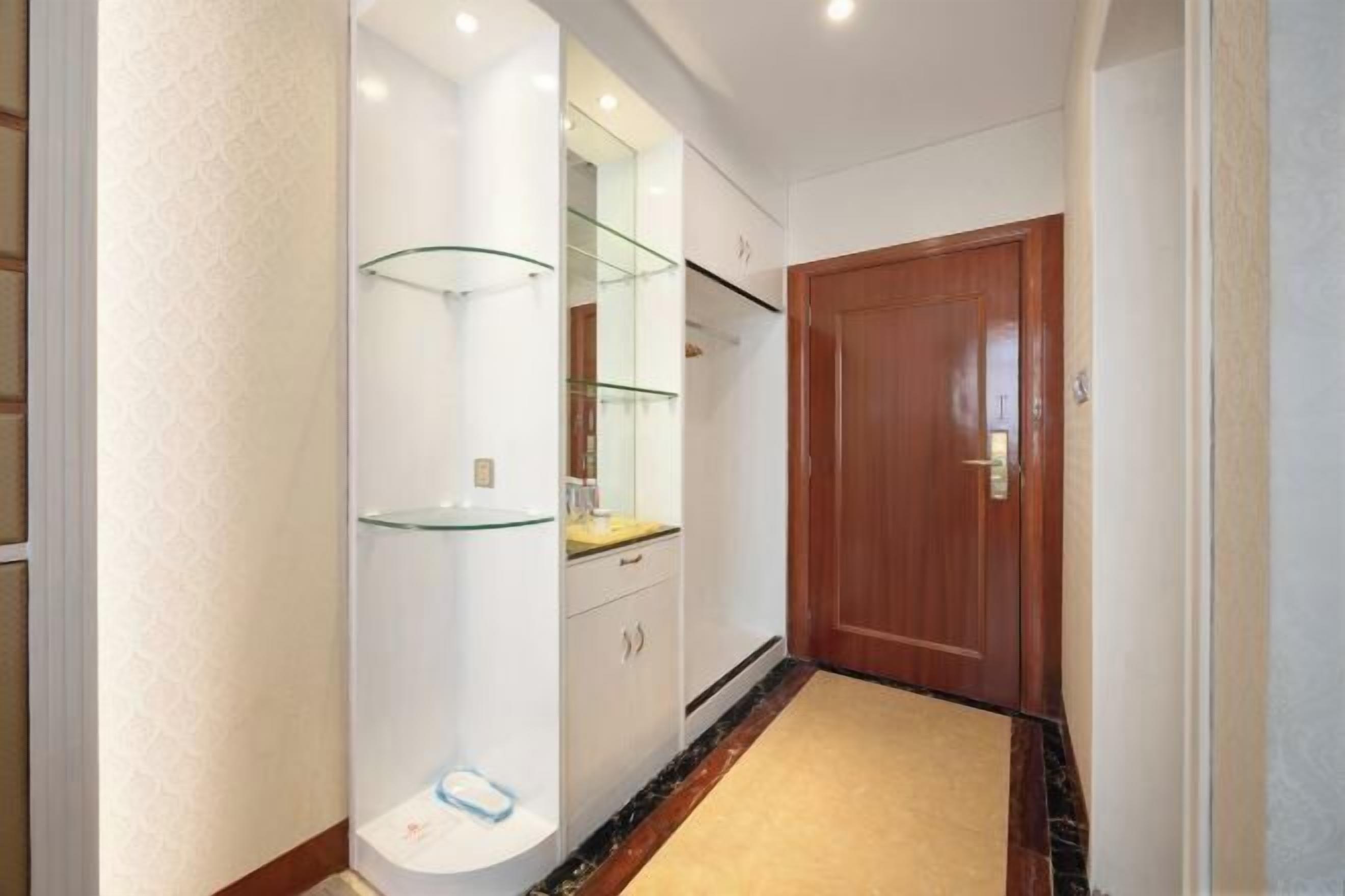 A hallway with a wooden door, a glass shelf unit, and a carpeted floor.