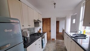 Uma cozinha com armários brancos, uma geladeira azul, painel de azulejos e piso de pedra.