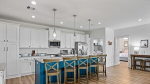 Una cocina moderna con armarios blancos, una isla azul y taburetes de madera.