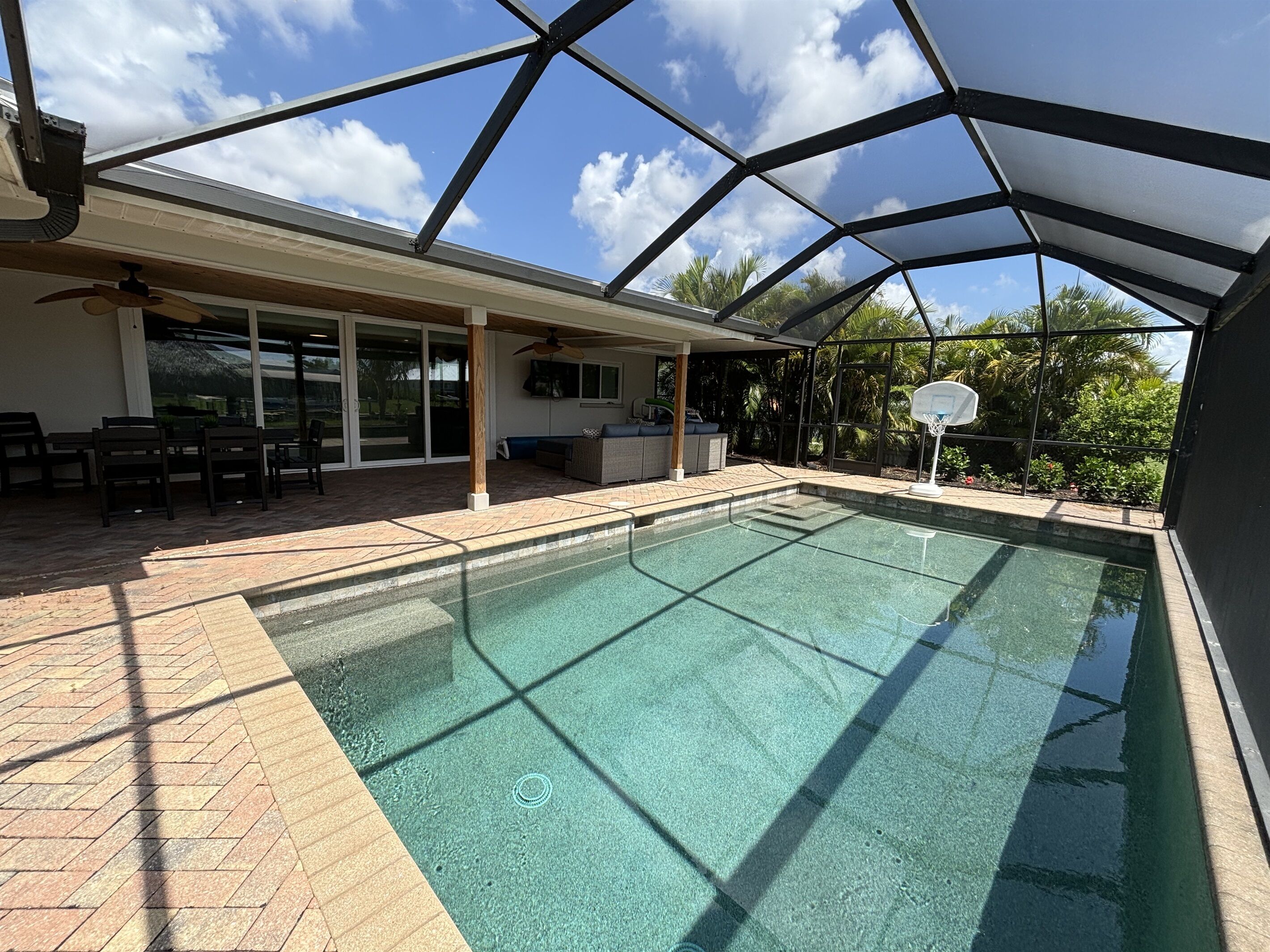 Une piscine intérieure dotée d’un toit en verre, un espace patio aménagé avec des sièges et un panier de basketball.