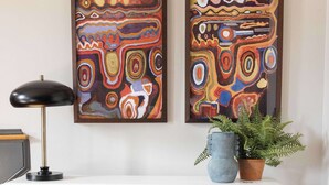A modern living room with a sofa, a white console table, abstract paintings, a lamp, a potted plant, and a decorative item on the console table. - Renovated Townhome Near Forsyth Park | Parking (Savannah)