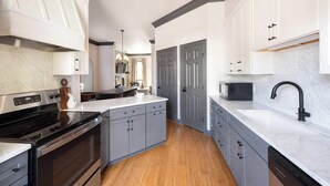 A modern kitchen with grey cabinets, a black stove, and a white countertop. - Renovated Townhome Near Forsyth Park | Parking (Savannah)