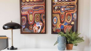 A modern living room with a sofa, a white console table, abstract paintings, a floor lamp, a potted plant, and a decorative item on the console table. - Renovated Townhome Near Forsyth Park | Parking (Savannah)