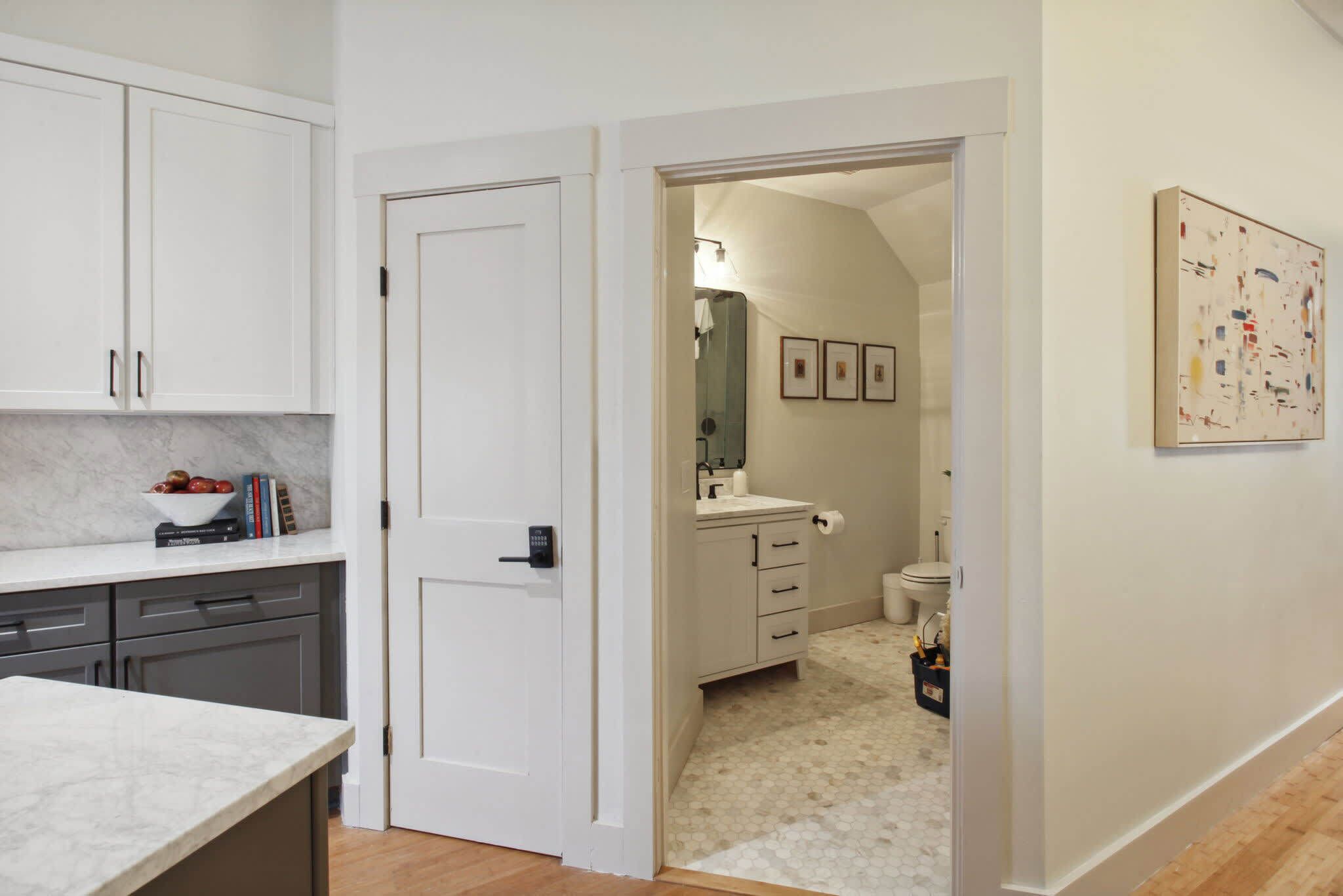 Una cocina moderna con encimeras de mármol, una puerta blanca y un pasillo que conduce a un baño con inodoro y lavamanos.
