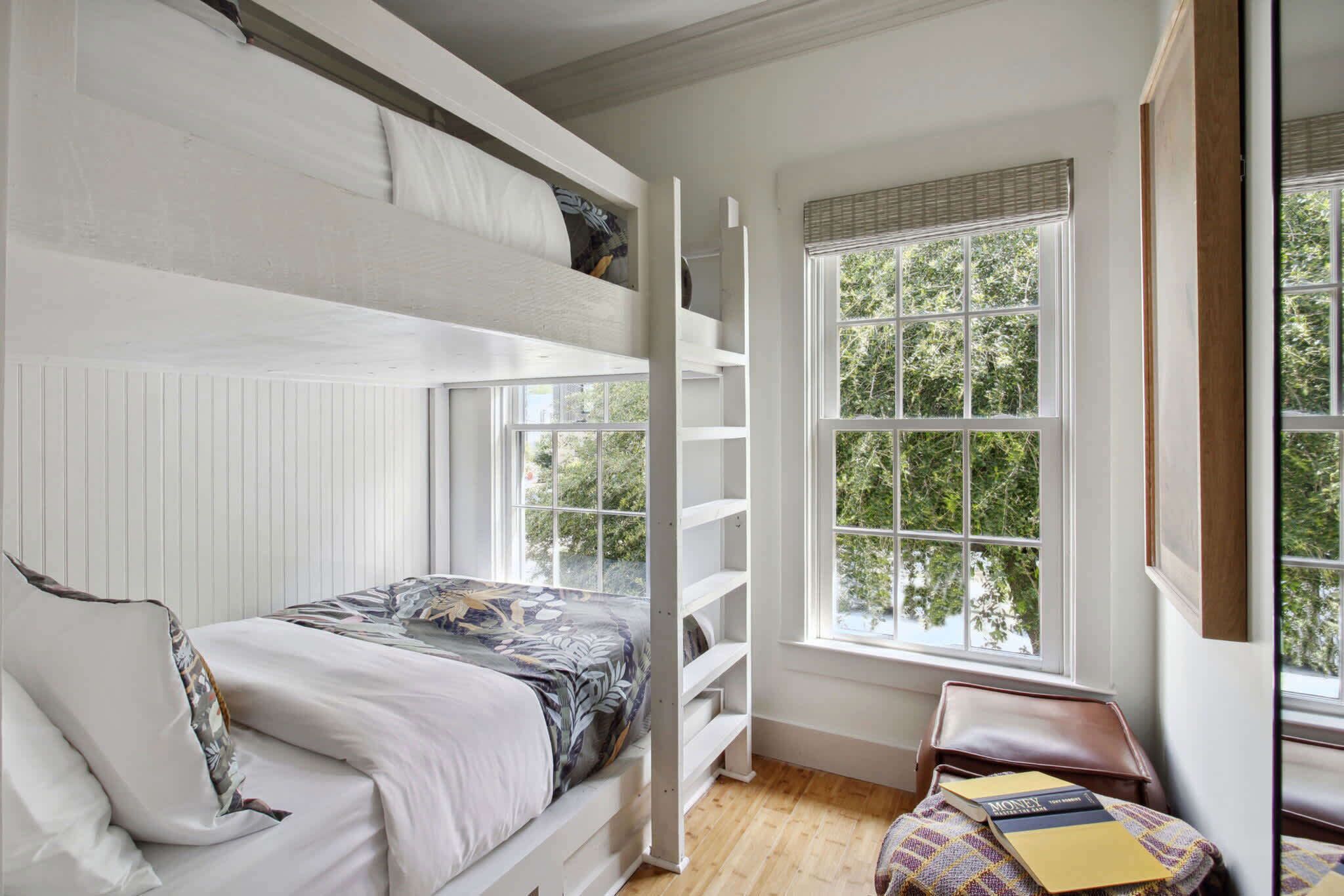 A bedroom with a bunk bed, a window with blinds, and a small table with a book.