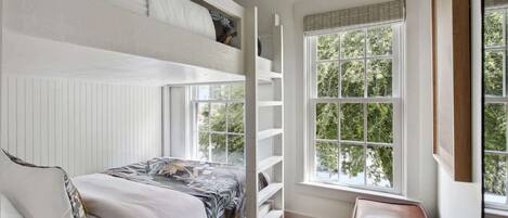 A bedroom with a bunk bed, a window with blinds, and a small table with a book.