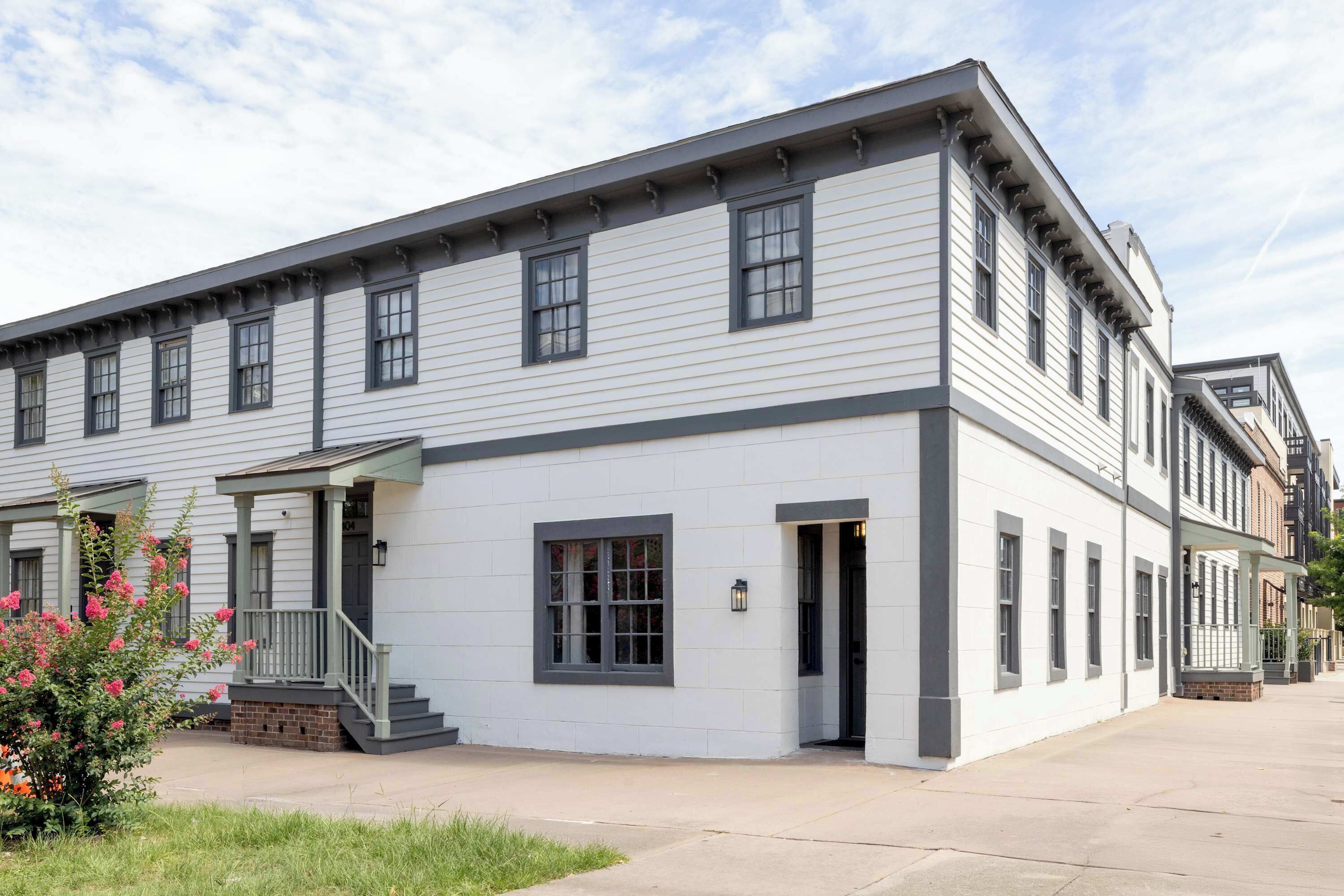 A two-story building with a white facade and dark trim, featuring a covered front porch and a brick base.