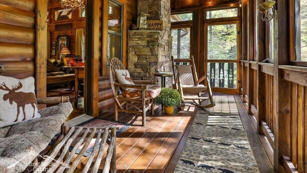 L’intérieur chaleureux d’un chalet en rondins, avec une cheminée en pierre, des meubles en bois et une vue sur la forêt.