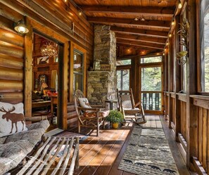 A cozy log cabin interior with a stone fireplace, wooden furniture, and a view of the forest. - Rushing Rapids at IttaBena Lodge, No Pet Fees, Sleeps 8, Creekfront Fishing (Ellijay)