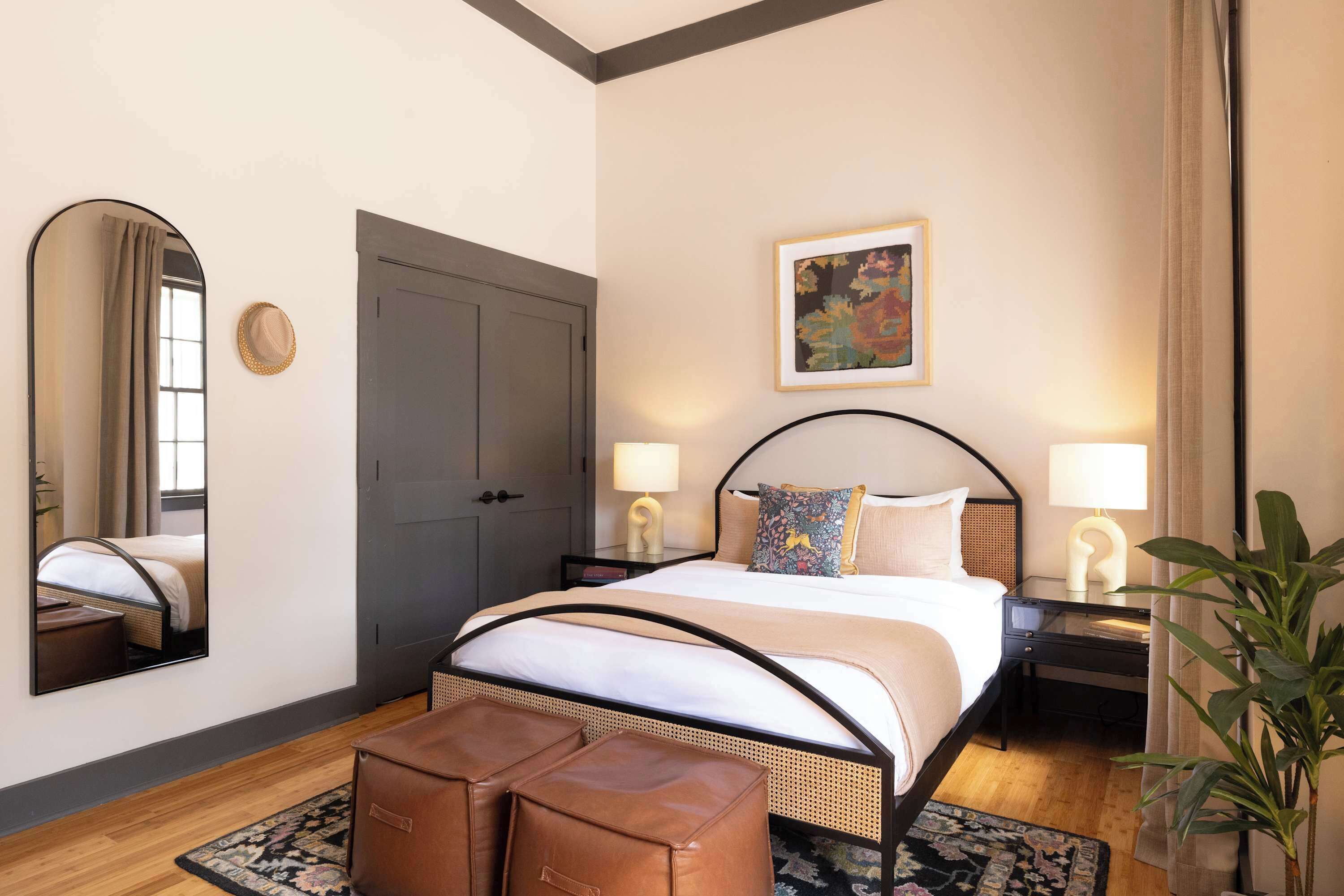 A bedroom with a bed, two bedside tables, a mirror, a door, and a potted plant.
