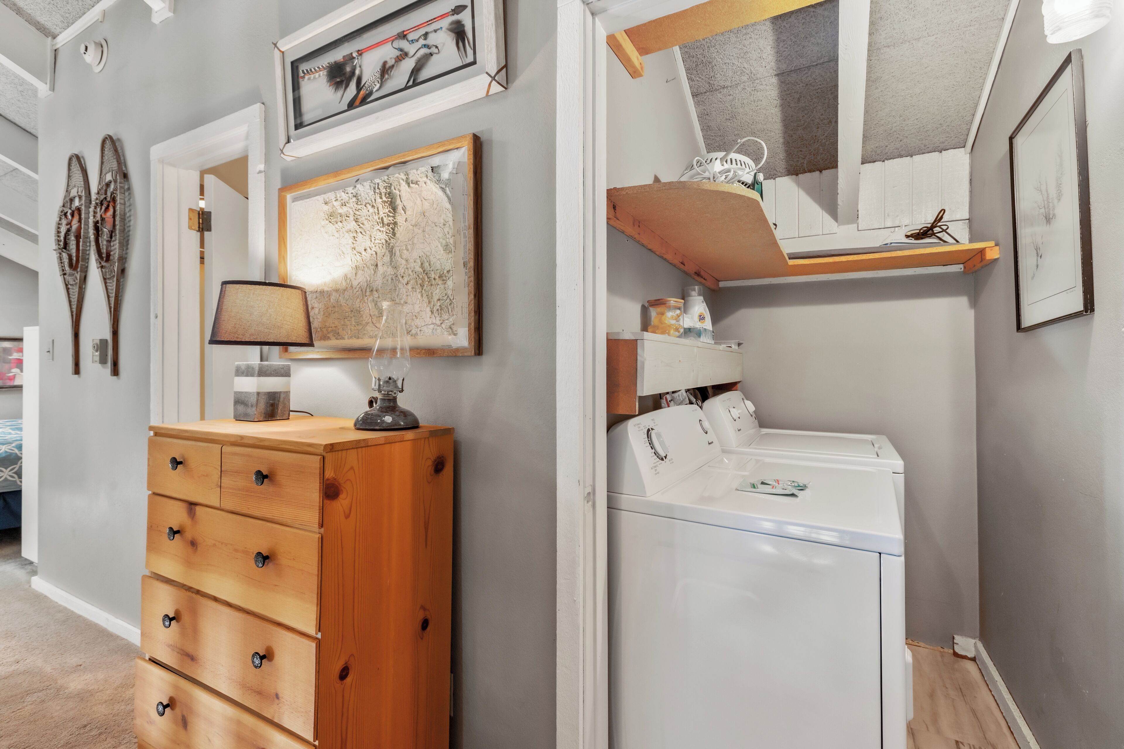 Une buanderie équipée d’une commode en bois, d’un lave-linge et d’une étagère où sont rangés divers objets.