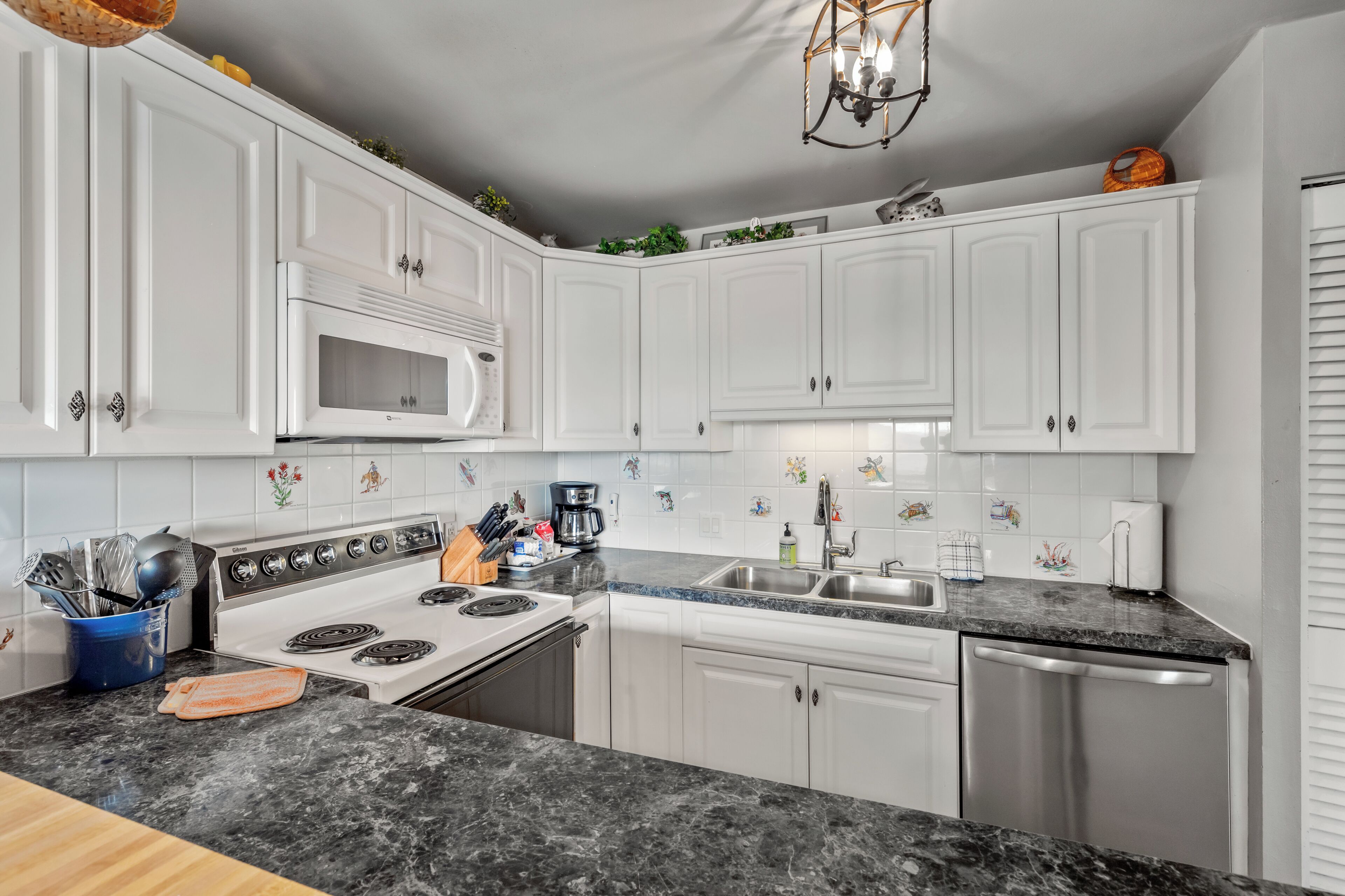 A modern kitchen with white cabinets, a granite countertop, a stainless steel dishwasher, and a built-in microwave.