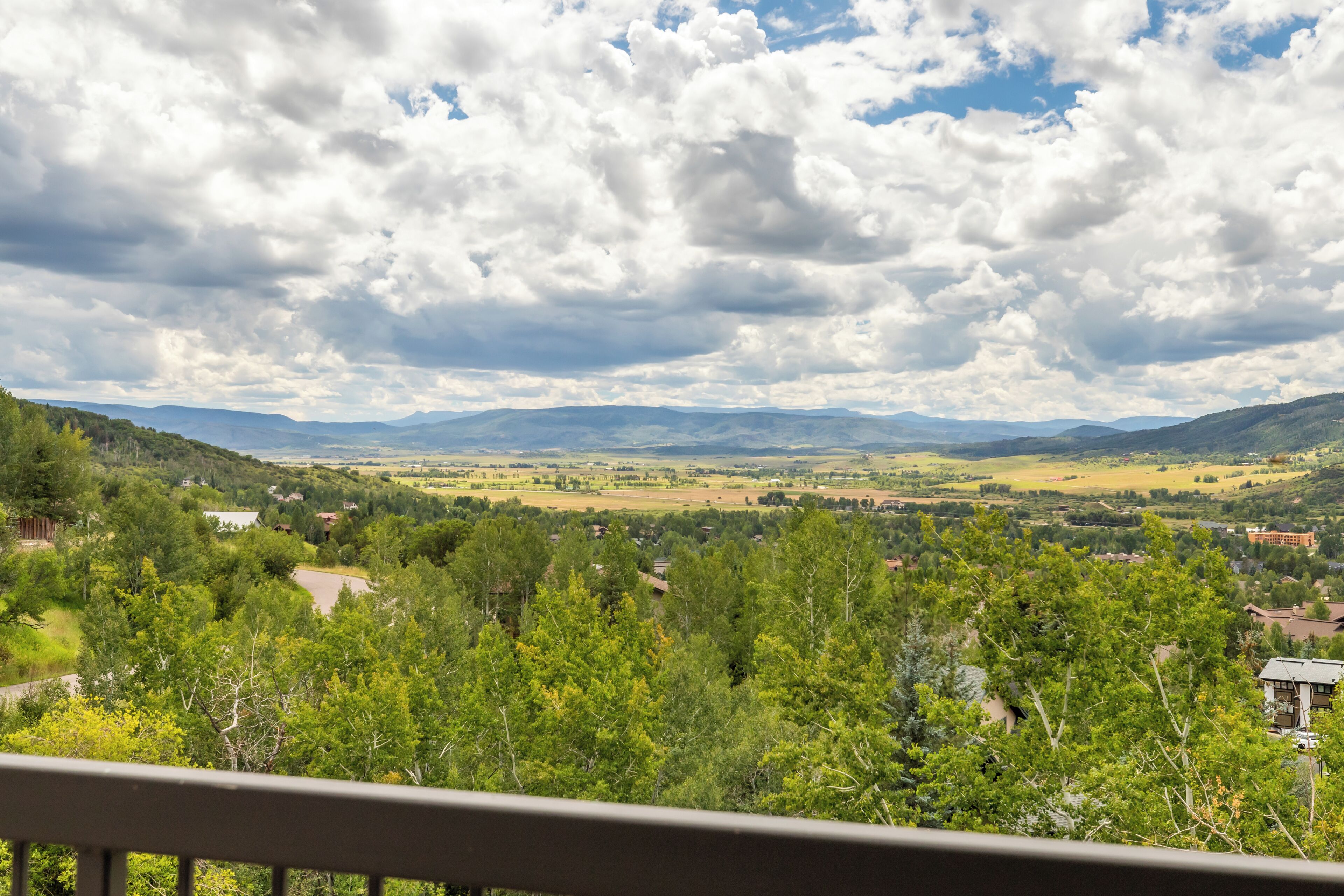 Una vista panoramica da un balcone su una valle con montagne sullo sfondo, case e alberi.