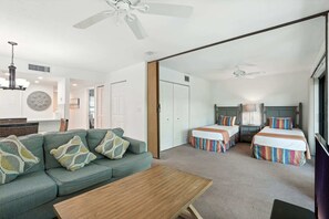 Ein Hotelzimmer mit einer Couch, zwei Betten, einem Holztisch und Deckenventilatoren.