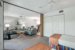 A living room with a sofa, coffee table, and a TV. There is a door leading to another room.