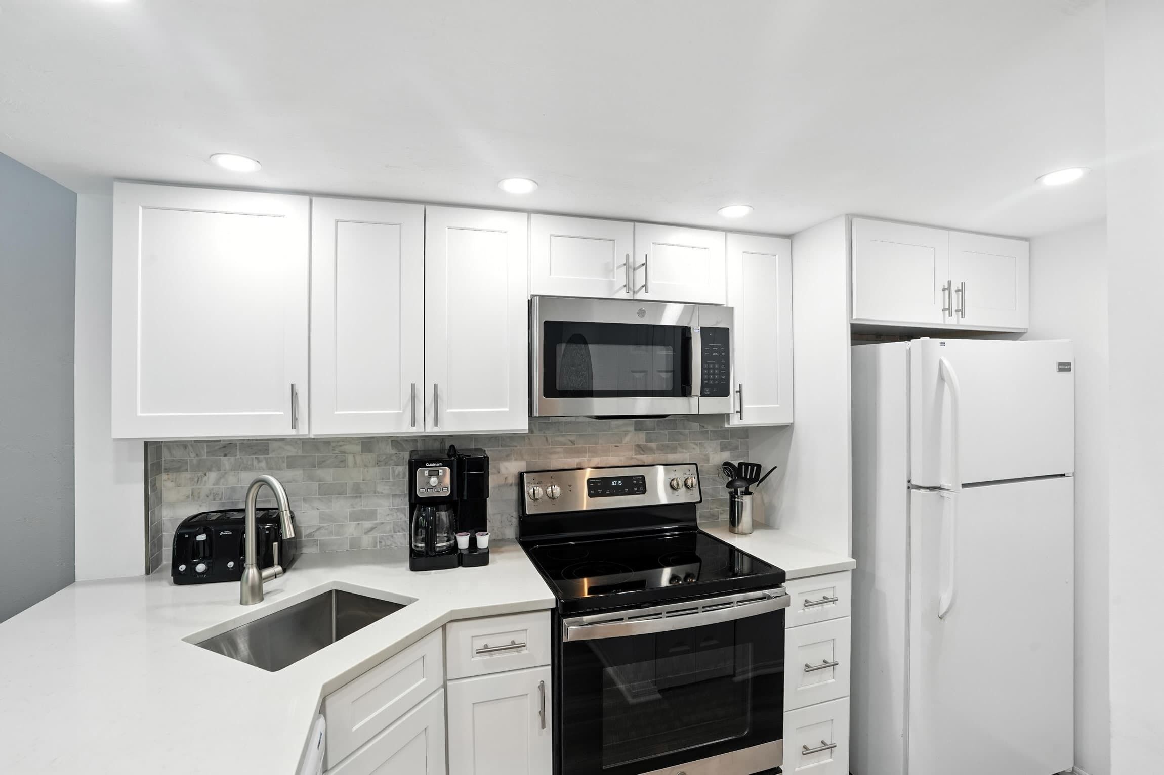 Une cuisine moderne avec des meubles blancs, un four à micro-ondes en acier inoxydable, une cuisinière noire et un réfrigérateur blanc.