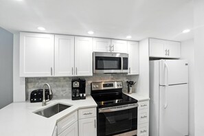 A modern kitchen with white cabinets, a stainless steel microwave, a black stove, and a white refrigerator.