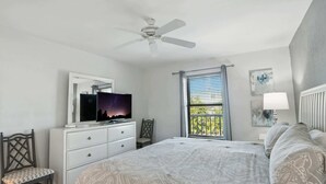 A bedroom with a bed, a dresser, a TV, a ceiling fan, a window with blinds, and a chair.