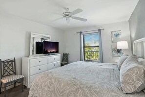 A bedroom with a bed, a dresser, a TV, a ceiling fan, a window with blinds, and a chair.