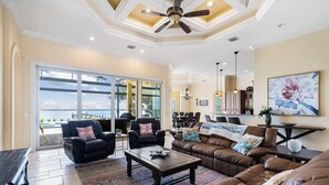 A spacious living room with leather sofas, a coffee table, and a large window with a view. - Peace River Waterfront Luxury Living - 5-BD w Pool (Port Charlotte)