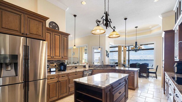 A spacious kitchen with a large island, stainless steel appliances, wooden cabinets, and pendant lighting. - Peace River Waterfront Luxury Living - 5-BD w Pool (Port Charlotte)