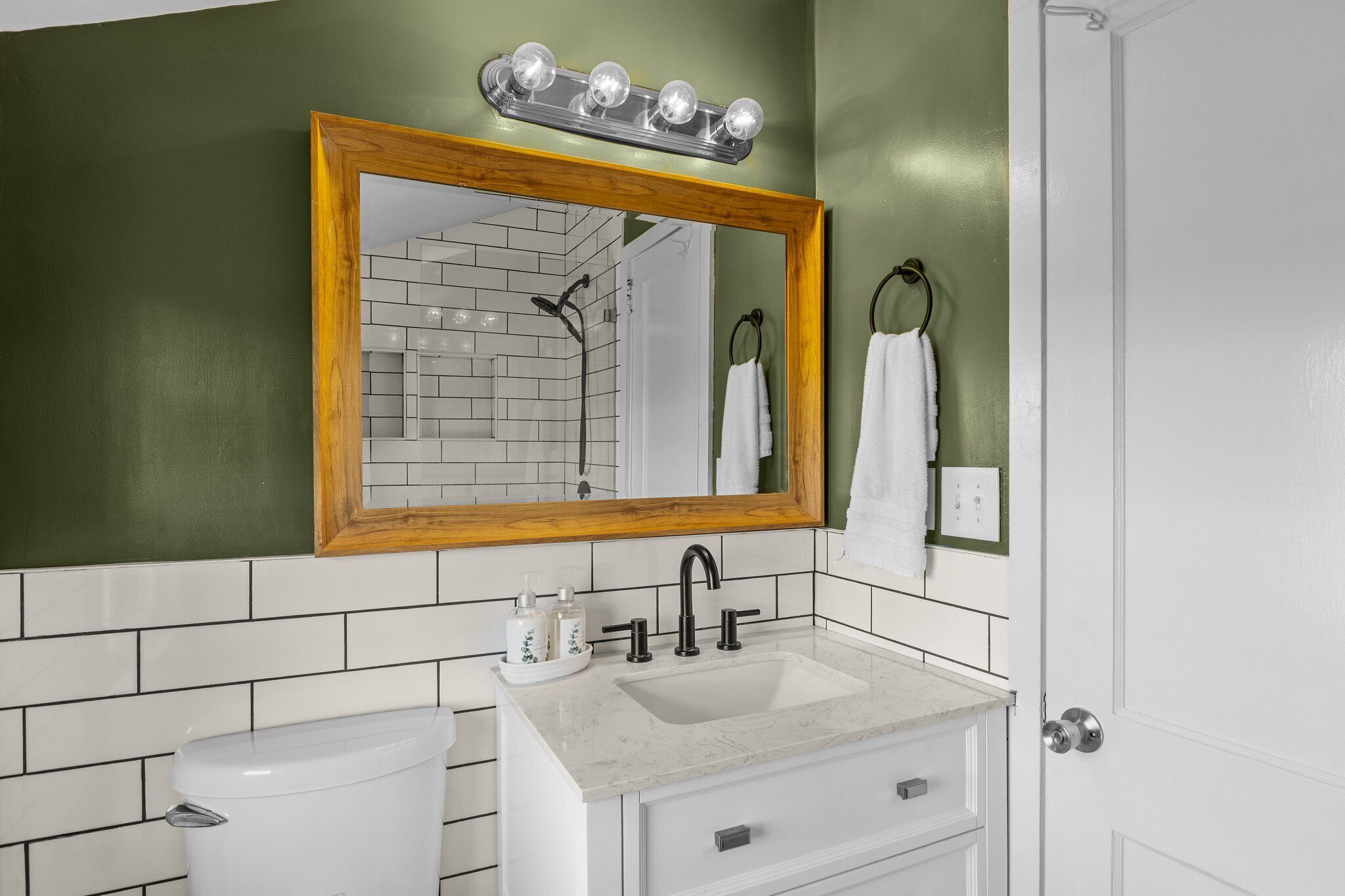 Une salle de bain avec un lavabo blanc, un miroir encadré en bois et un mur vert.