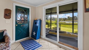 Een kamer met een blauwgroene deur, een blauw voorwerp dat ertegen leunt, uitzicht op een grasveld door een schuifdeur, en een kamerbreed tapijt op de vloer.