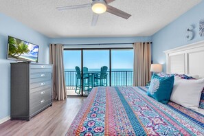 Ein Schlafzimmer mit Bett, Kommode, Fernseher und einem Balkon mit Sitzgelegenheiten, mit Blick auf den Ozean.