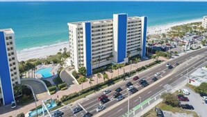 A high-rise hotel with a pool, located near a beach and a busy road. - Ocean Sands 1-1002☀️Beachfront,Private Balcony,Walk 2 Restaurants🏖️Beach Access (Madeira Beach)