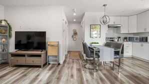 A modern living room with a TV, entertainment unit, and dining area with a table and chairs. - Winston Suite 2BR 1BA - Carriage Suite with Garage (Calgary)