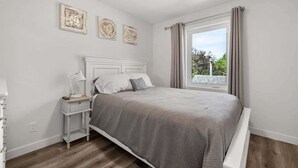 A bedroom with a bed, bedside table, lamp, and artwork on the wall. - Winston Suite 2BR 1BA - Carriage Suite with Garage (Calgary)