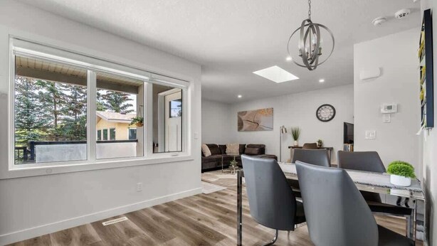 A modern dining area with a large window, a chandelier, and a dining table with chairs. - Winston Suite 2BR 1BA - Carriage Suite with Garage (Calgary)