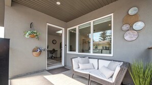 An outdoor seating area with a wicker sofa, a potted plant, and a wall-mounted decorative piece. - Winston Suite 2BR 1BA - Carriage Suite with Garage (Calgary)