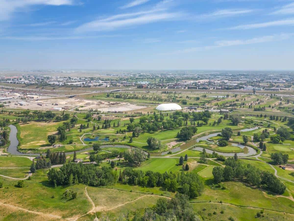 Vista aérea de un campo de golf con una estructura abovedada grande, rodeado de campos verdes y árboles.