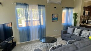 A living room with a grey sofa, a black coffee table, and a TV on a stand. - Charming 2-bedroom townhome with WiFi, AC in beautiful Ocho Rios (Ocho Rios)