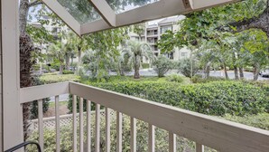 A balcony with a view of a landscaped garden, a palm tree, and a building in the background. - Sunset Rentals | Continental Club 1 (Hilton Head Island)