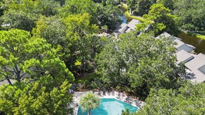 An aerial view of a residential area with a swimming pool surrounded by lush greenery and a river. - Sunset Rentals | Ocean Cove 826 (Hilton Head Island)