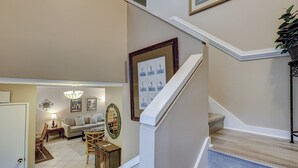 A staircase with a wooden finish and white trim, leading to a living area with a sofa, chairs, and a dining table. - Sunset Rentals | Ocean Cove 826 (Hilton Head Island)