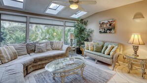 A spacious living room with a high ceiling, skylights, a large window, and a ceiling fan. - Sunset Rentals | Ocean Cove 826 (Hilton Head Island)