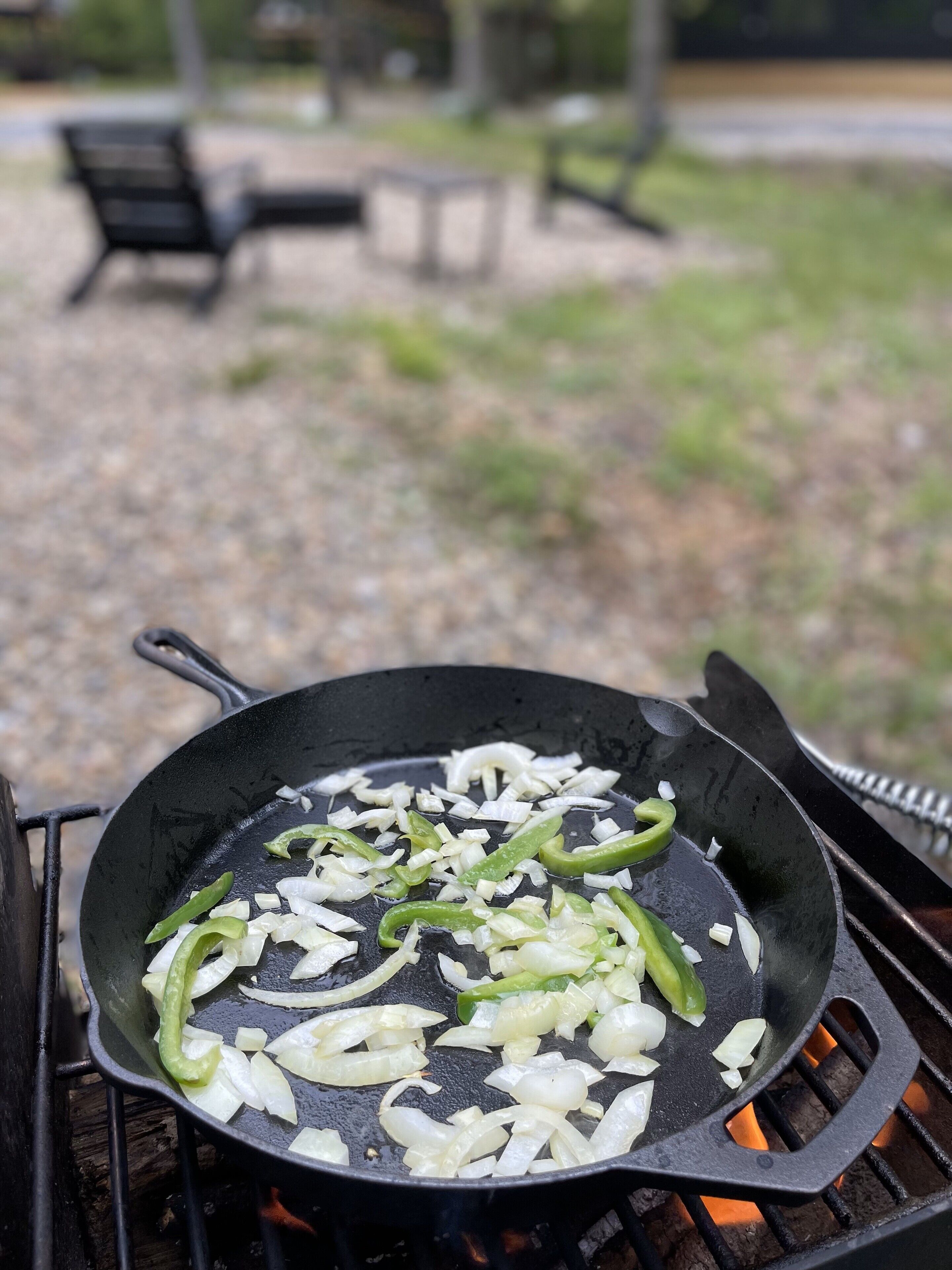 A skillet on an outdoor grill with chopped onions and green peppers.