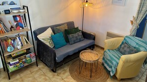 Una sala de estar acogedora con un sofá, una silla, una lámpara y una estantería llena de libros y juegos.