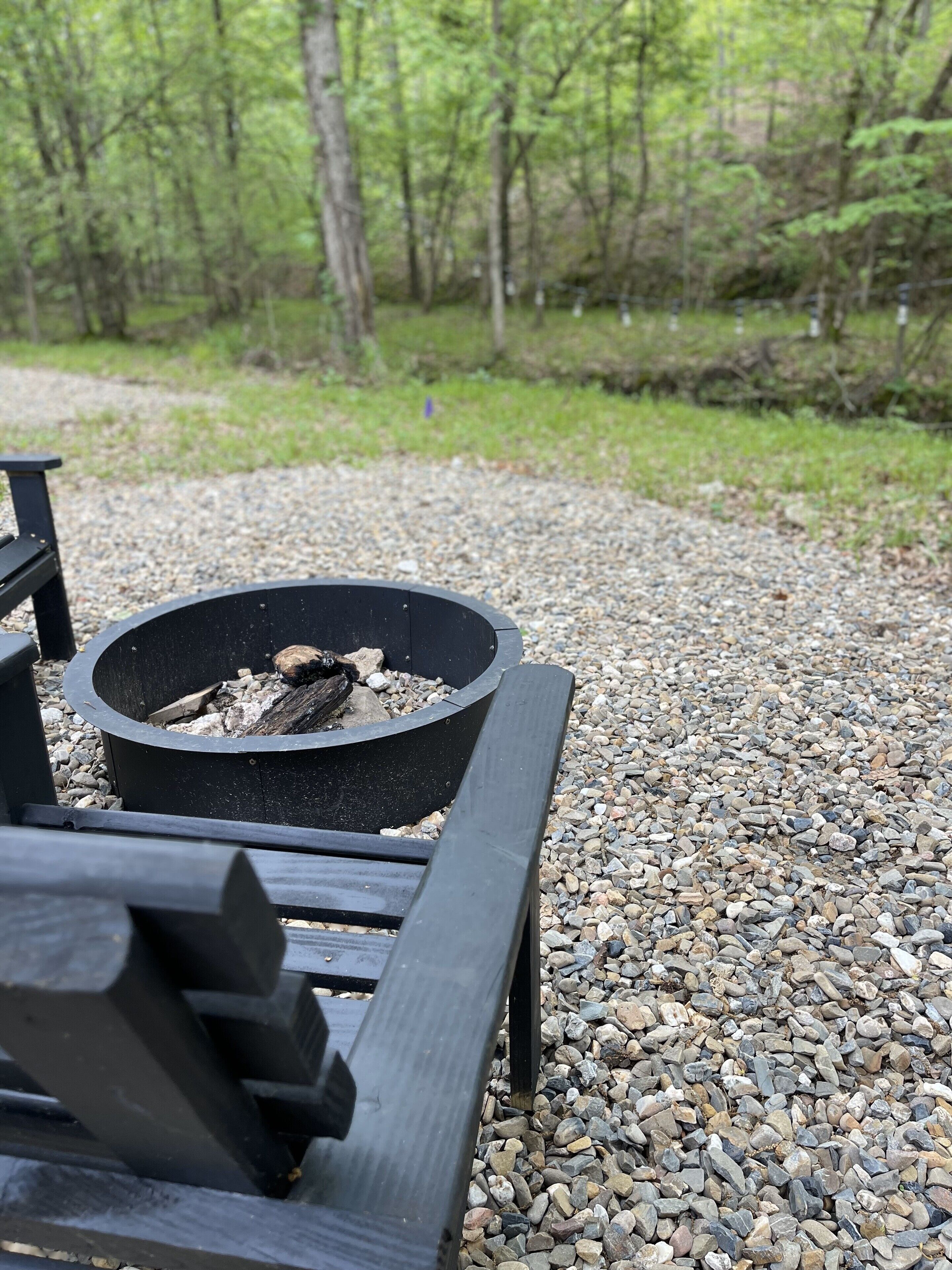 A fire pit with logs, surrounded by a gravel area with a wooden bench nearby.