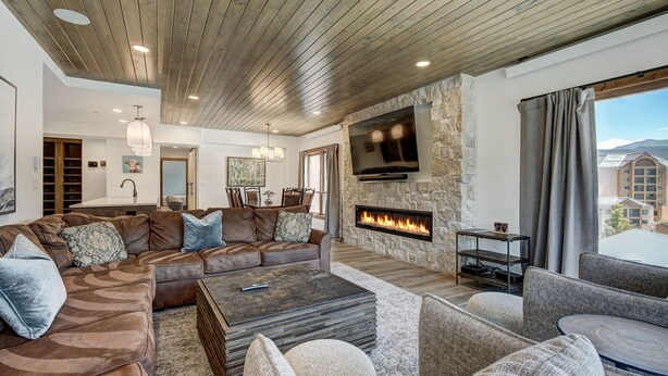 Un salón espacioso con chimenea de piedra, sofás de cuero y un televisor grande montado en la pared.