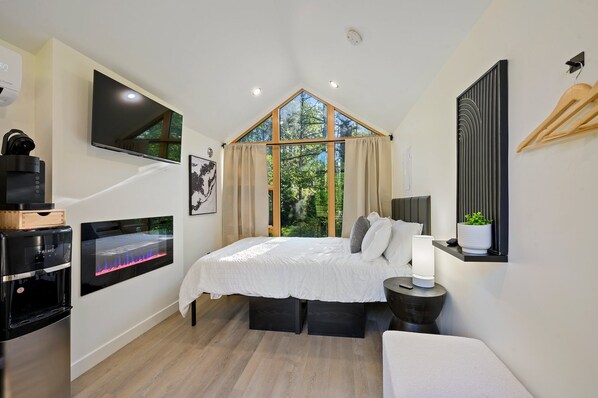 Un dormitorio con una cama grande, un televisor montado en la pared, un dispensador de agua y una ventana con cortinas.