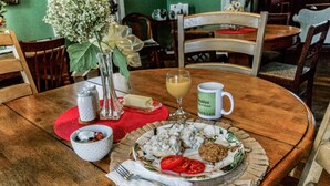 Une table de salle à manger en bois, avec une assiette de nourriture, un verre de jus de fruits et un vase rempli de fleurs.