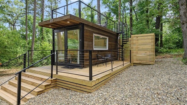 Una cabaña de madera con puerta de cristal, una terraza de madera y una escalera que lleva a un balcón.
