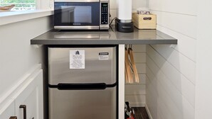 Una kitchenette compacta con microondas, cafetera y refrigerador.